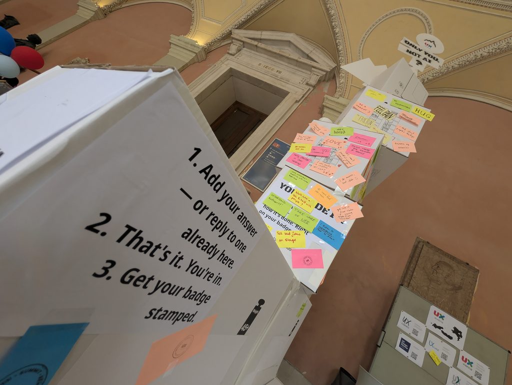 Looking up along the tower from its base: printed instructions on a box in the foreground and note-covered boxes rising toward the vaulted ceiling.